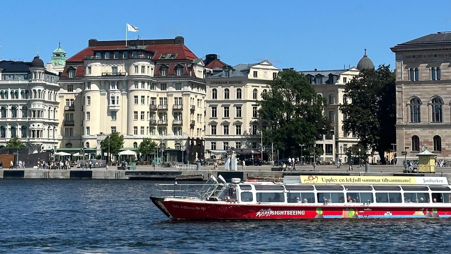 A tour boat cruises past historic waterfront buildings in Stockholm on a sunny day.